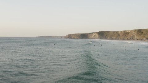 Low flight over the seas of Cornwall, showing the surfers out during sunset, waiting their chance to get on the next set of waves that roll in.