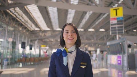 Beautiful and attractive Caucasian flight attendant staff smiling and walking with confidence face and happiness in airport terminal to the airplane. Cabin crew or hostress occupation concept.
