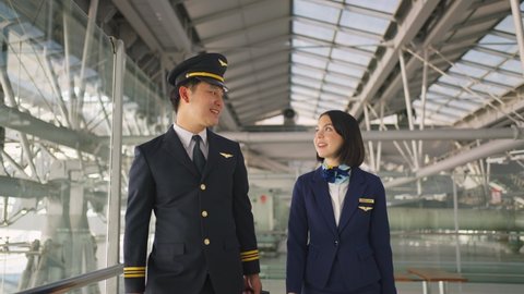 Asian airliner pilot and air hostess walking and talking together in airport terminal to the airplane with smile face and happiness. Commercial cabin crew or hostress and pilot occupation concepts.