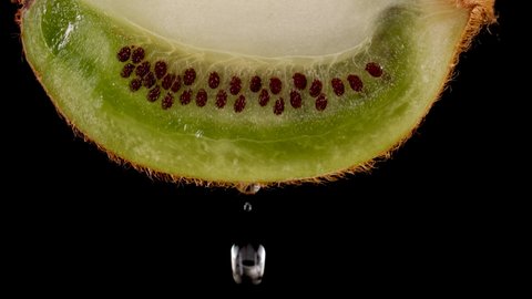 Macro Shot Drop Of Water Dripping Slice of fresh Green Kiwi and Seeds Fruit on Black Background. Slow Motion Water Drop From Juicy Fresh Ripe Delicious Sliced Kiwi Fruit, Close-up Slow Motion.