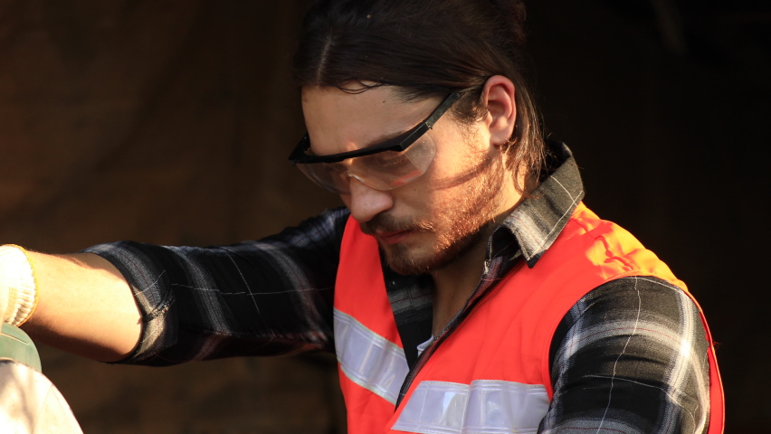 Handsome young caucasian carpenter using table saw cutting wood on construction site.