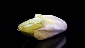 Chicory salad rotating on a black background in 4K. Close up of fresh Belgian endive, studio footage.