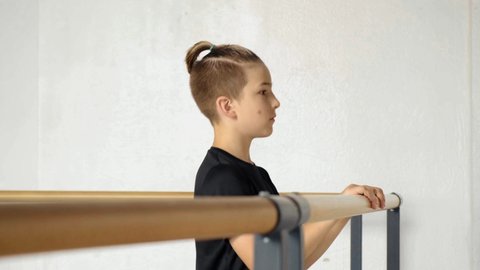 A young guy stands in front of the mirror and stretches his feet before a sports activity. Dance ballet. Hands on the barre. Man learning to dance ballet.