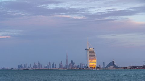 Dubai skyline with downtown skyscrapers during sunset day to night transition timelapse. View from palm artificial island in front of kite beach.