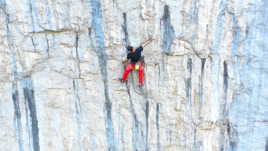 Young fit man climbing on very steep mountain cliff, outdoors rock climbing and active lifestyle concept. Camera movement reveals the mountain wall cliff. Extreme sports concept. Rocky Mountains. | Shutterstock HD Video #1066631716