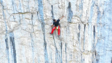 Young fit man climbing on very steep mountain cliff, outdoors rock climbing and active lifestyle concept. Camera movement reveals the mountain wall cliff. Extreme sports concept. Rocky Mountains.