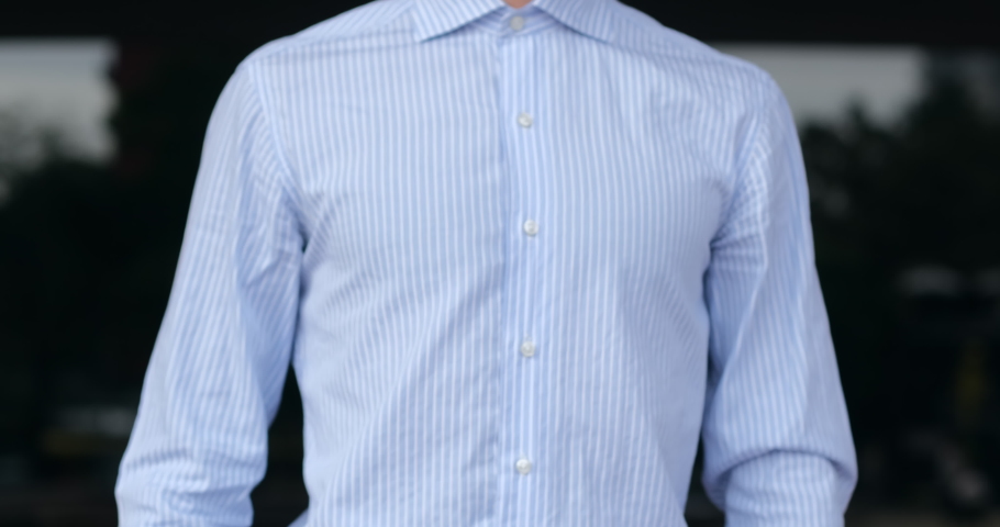 A man in a shirt holds his mobile phone in his hand and quickly swipes his finger across the screen, outdoors against the dark windows. Fast 5G mobile internet. Medium shot without face.