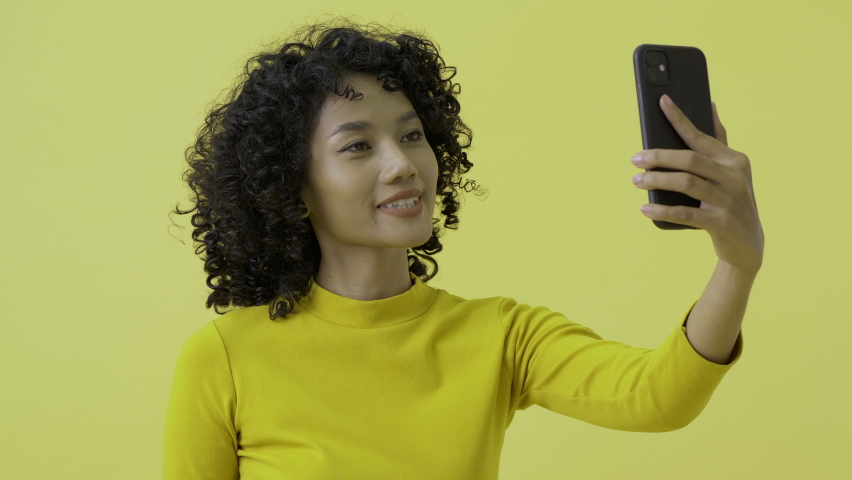 Young woman using smartphone to talking with friend. She using video call to talk at yellow background.