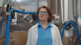Portrait of confident female scientist in lab coat walking in modern beer factory. Young woman engineer wearing white coat inspecting brewery plant with large steel tanks - Powered by Shutterstock - Get 15% off with code: PIKWIZARD15