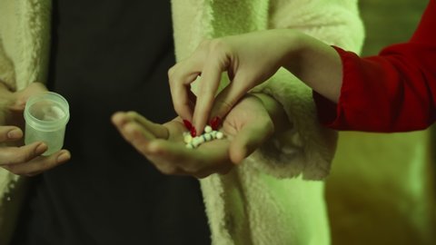 Close up of man pouring drug pills on hand and giving to woman in nightclub. Drug dealer providing customer female with lsd at party. Drug addiction concept