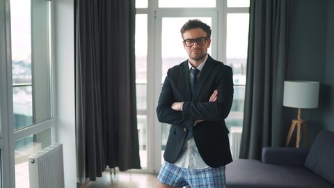 Portrait of a Caucasian man in glasses, a jacket and underwear in the interior of a modern home. Remote work during a pandemic