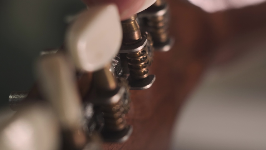 Man is tuning musical instrument. The musician twists the guitar tuner pegs and pulls the strings to start playing music. Extreme close up footage with grain. | Shutterstock HD Video #1066636702