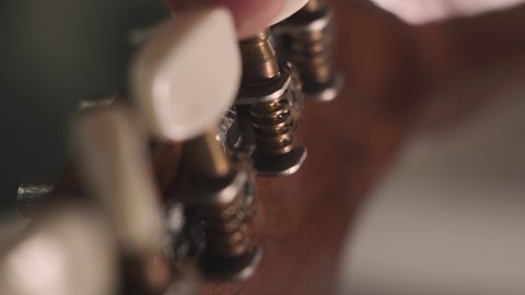 man is tuning musical instrument. The musician twists the guitar tuner pegs and pulls the strings to start playing music. Extreme close up footage with grain.