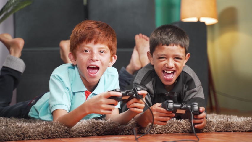 Two multi ethnic kids busy in playing videogame using gamepad while lying on floor at home - Concept of children unhealthy playing position and new technology addiction | Shutterstock HD Video #1066639330