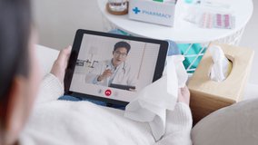 Over shoulder view of young asia woman talk to doctor on cellphone videocall conference medical app in telehealth telemedicine online service hospital quarantine social distance at home concept.