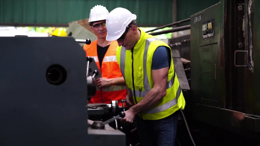 Engineer And Apprentice Using Automated Milling Machine. Worker with goggles and helmet on the machine.