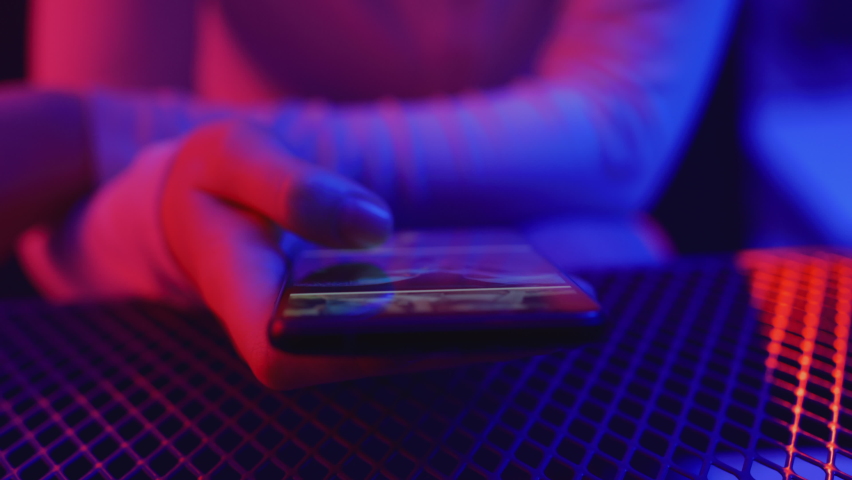 Use of mobile phone in shining neon light. Creative vivid color of ultraviolet red and blue. Hands of person scrolling up photos of instagram. Stylish social media photograph close-up at neon art room Royalty-Free Stock Footage #1066645474