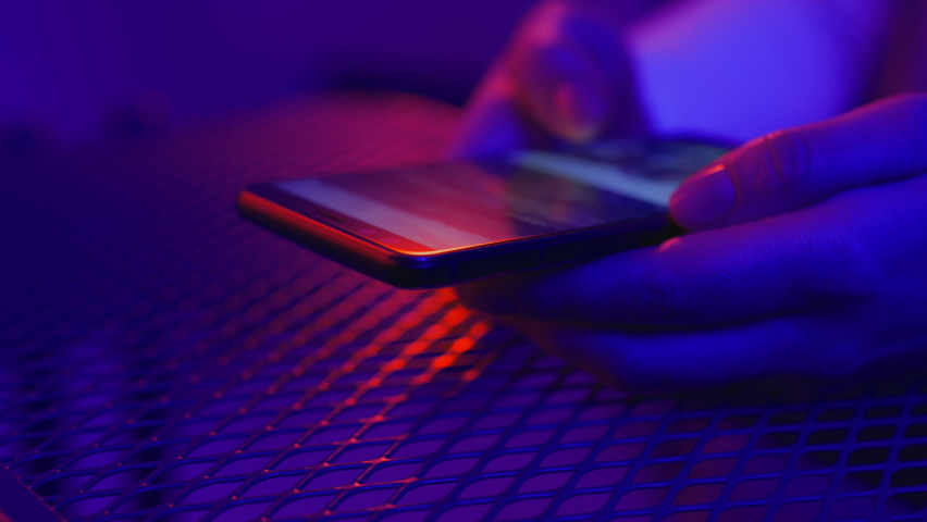 Use of mobile phone in shining neon light. Creative vivid color of ultraviolet red and blue. Hands of woman scroll up photos of instagram app. Social media photography closeup at party in night club Royalty-Free Stock Footage #1066645477