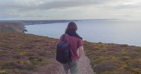 Long Haired Man With Backpack Walking At The Coast Of Wheal Coates In Cornwall, England - back view - wide slowmo shot