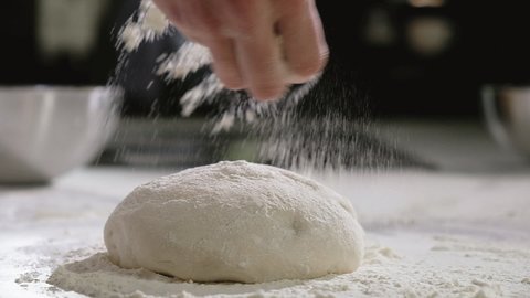 Baker prepares dough for traditional Italian pizza. chef in bakery makes morning dough for baking pizza sprinkles flour on dough. Cooking traditional Italian pizza in restaurant kitchen. close-up