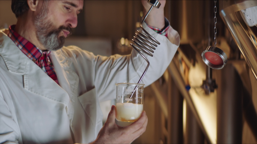 Quality brewing expert taking sample of beer from big brewery vat. Quality control in brewing process. Factory, brewery concept.