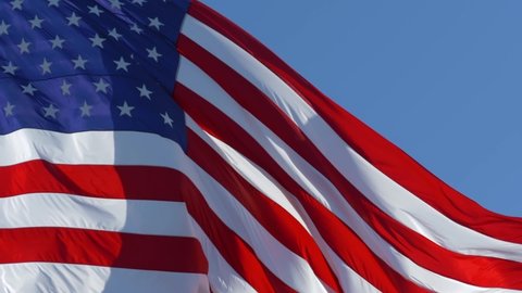 SLOW MOTION, CLOSE UP: American Flag Waving in the Wind. Close up of large American flag waving in front of blue sky. Close up of an American flag flying in the wind against a background of clear sky.