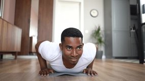 Front view of cheerful African-American man doing push-up on floor at bright living room, looking at camera. Concept of sport workout training at home gym. Shooting in slow motion. - Powered by Shutterstock - Get 15% off with code: PIKWIZARD15