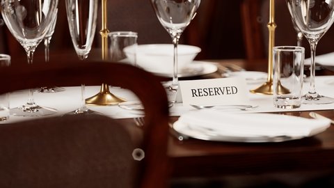 Reserved table card closeup. Animation of elegant tableware at a restaurant. Dinner set at the wedding reception. Plates, napkins, glasses, flatware on the wooden table. Ready for celebration. 4 K HD