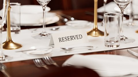 Reserved table card closeup. Animation of elegant tableware at a restaurant. Dinner set at the wedding reception. Plates, napkins, glasses, flatware on the wooden table. Ready for celebration. 4 K HD
