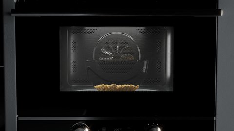 Animation of corn seeds popping up from rotating glass bowl at the microwave. Delicious salty snacks ready to eat while watching a movie at home. Popcorn preparation. A black oven. Dark background. 4K