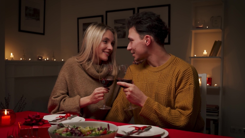 Happy young couple in love hugging, laughing, drinking wine, enjoying talking, having fun together celebrating Valentines day dining at home, having romantic dinner date with candles sitting at table. Royalty-Free Stock Footage #1066667017