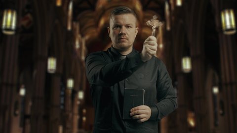 Closeup portrait of a young catholic praying priest on the background of the church.Priest holding is dressing in black, holding a crucifix,baptizing the room and reading New Testament book.