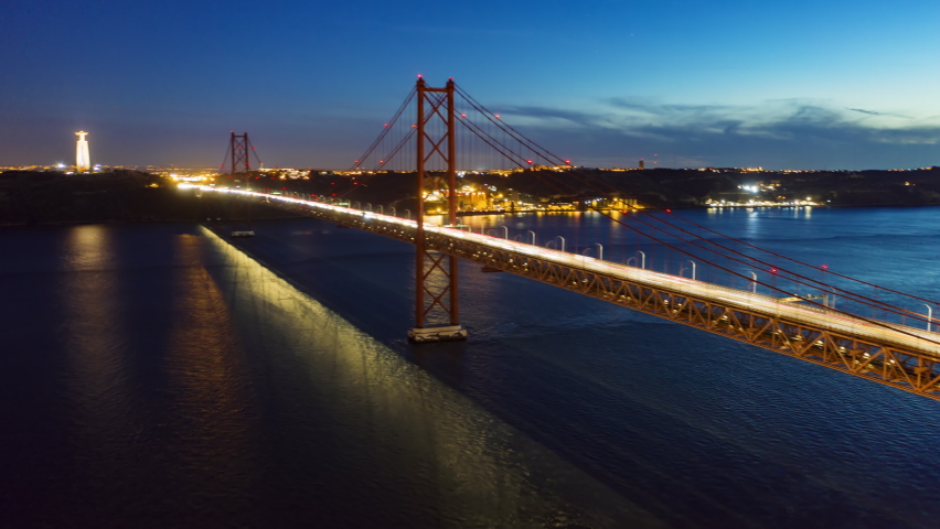 Drone flying over Ponte 25 de Abril at night, Lisbon, Portugal, Europe. Aerial view of cars driving on bridge in night time. Suspension bridge over Tagus river in Lisbon. 4k footage in hyperlapse Royalty-Free Stock Footage #1066668253