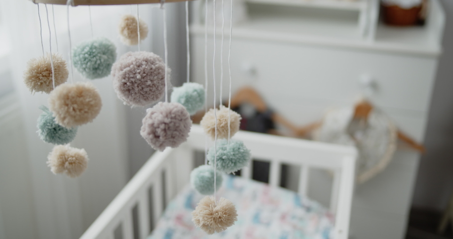 Handmade baby mobile toy hanging spinning above the crib in the bedroom. Close-up shot of multi colored nursery mobile in front of the baby changing table. Concept of childhood, new life, parenthood. Royalty-Free Stock Footage #1066671118
