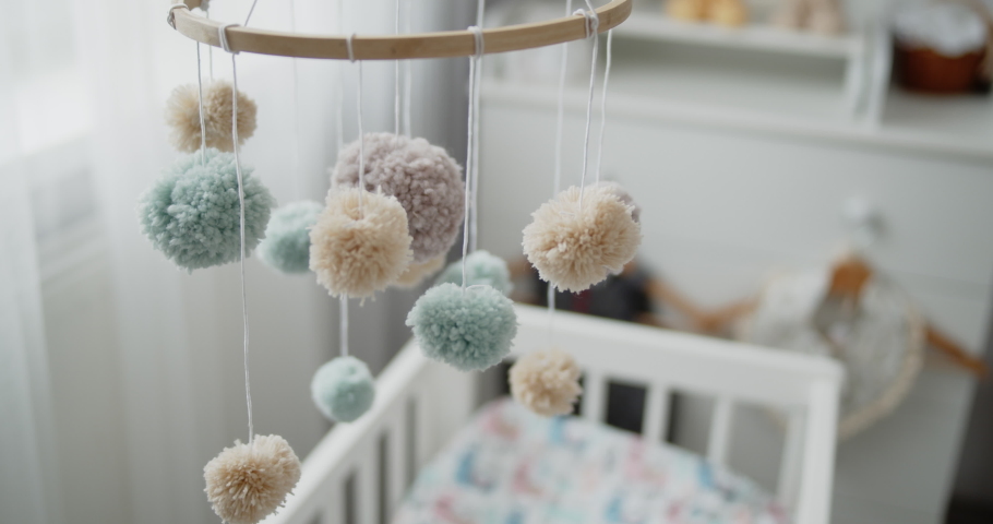 Handmade baby mobile toy hanging spinning above the crib in the bedroom. Close-up shot of multi colored nursery mobile in front of the baby changing table. Concept of childhood, new life, parenthood. | Shutterstock HD Video #1066671118