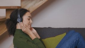 Music lover. Profile portrait of carefree african american lady listening to music in headphones, relaxing and dancing at home, slow motion