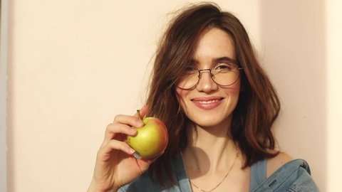 Young curly brunette woman hold apple and show thumb up, eating apple and smile. Bite fresh apple with happiness to diet, weight and calories control and good health lifestyle concept. Healthy teeth