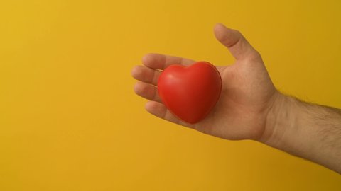 Young man's hand squeezes red anti-stress heart toy. Romantic love, calmness and peace, Saint Valentine's Day preparation design concept. Preparation for donation