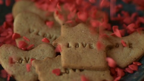 Red scarlet heart shaped sugar confetti crumbling and falling down on cookie with love written on it. Romantic love, affection Saint Valentine's Day, Mothers Day, wedding preparation design concept