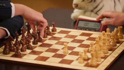 Chess grandmasters playing speed chess with a chess clock and a wooden chessboard.