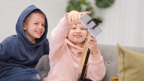 Kids bloggers talking with followers, live streaming looking to smartphone screen at home. Little boy and girl making selfie
