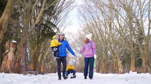 happy married couple with young children walking with sledges in a snowy park in winter. Young family Husband and wife with young sons spend leisure time together on the weekend