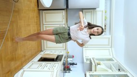 vertical video. beautiful girl dancer cheerfully dancing at home in the kitchen.
