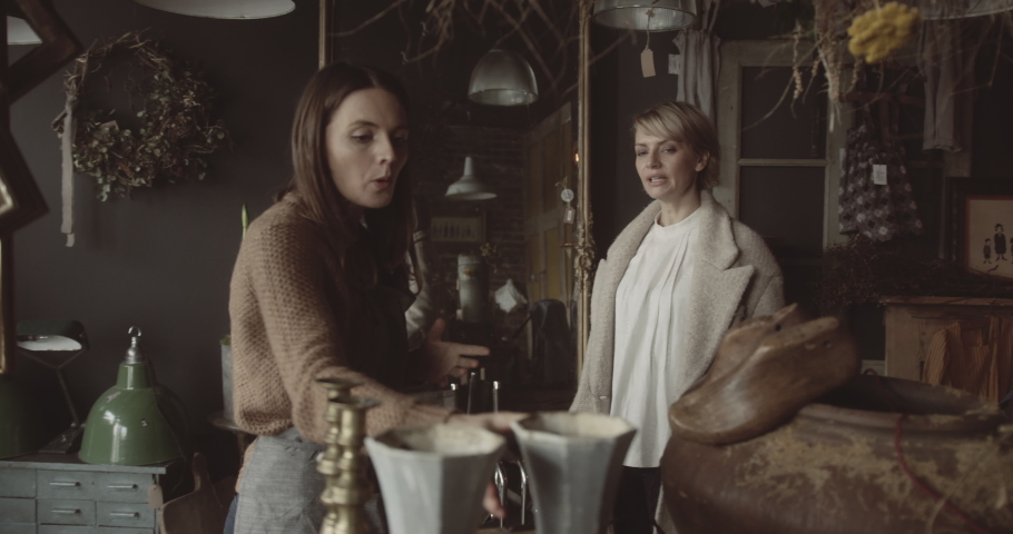 Retail clerk advising customer in antique shop and looking at vase