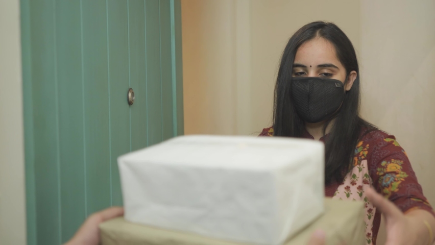 close view shot of beautiful young Indian woman with protective face mask receiving parcel which is being delivered at the doorstep of her apartment or residence and closes the door thereafter Royalty-Free Stock Footage #1066700746