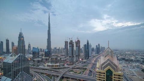 Modern skyscrapers and busy evening highways day to night transition timelapse in luxury downtown of Dubai city. Top aerial view from tower rooftop. Road junction traffic. Dubai, United Arab Emirates