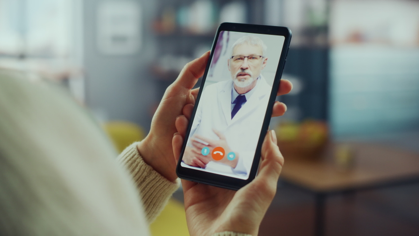 Close Up of a Female Chatting in a Video Call with Her Senior Family Doctor on Smartphone from Living Room. Ill-Feeling Woman Making a Call from Home with Physician Over the Internet. Royalty-Free Stock Footage #1066706794