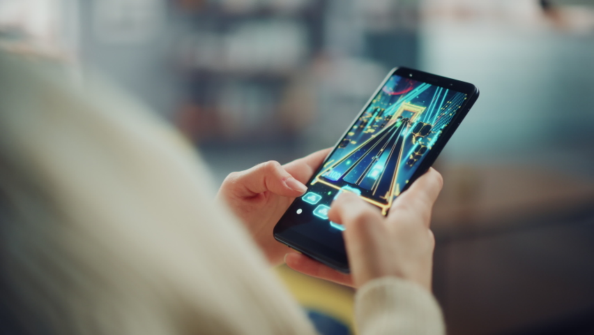 Close Up on a Person Hands Playing an Arcade Video Game on a Vertically Held Smartphone at Home Living Room. Feminine Hands Tapping the Mobile Phone Screen with a Colorful Game Over the Internet.