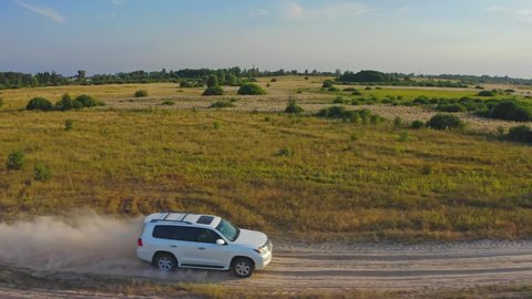 SLOW MOTION. AERIAL VIEW. White suv car is fast going on rural road. Drone is following to a car rides in cross country with a huge dust clouds. Fast moving car that leaves clouds of dust in its wake 