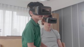 Young asian father and son sitting and playing video game virtual reality with fun on sofa in the room at home, man and boy doing activity hobby for relaxation on couch together, family concept.